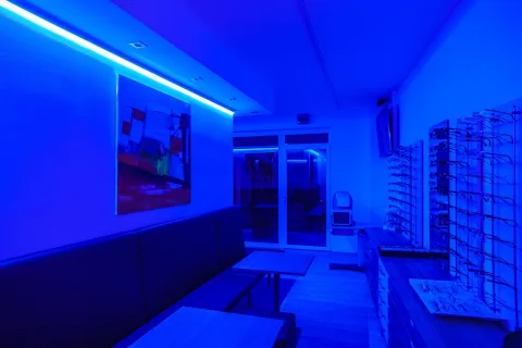 Verkaufsraum in blaues Licht getaucht, mit Sitzbank, Brillenregalen an der Wand und einem abstrakten Gemälde