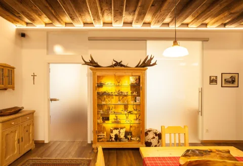 Beleuchteter Holzschrank voller Brillen unter einem Geweih, in einem Raum mit Holzdecke und Kreuz an der Wand