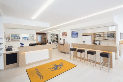 Heller Verkaufsraum mit langer weißer Theke, Barhockern und einem gelben Teppich mit Hirschmotiv