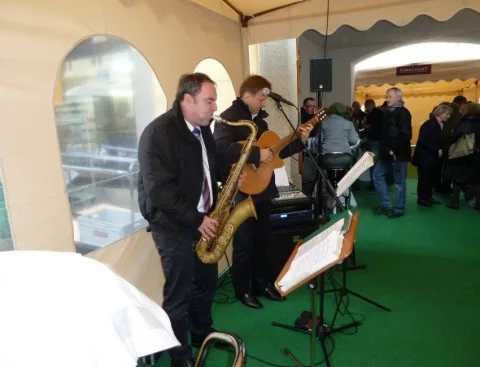 Zwei Musiker spielen Saxofon und Gitarre in einem Festzelt mit grünem Boden.