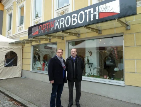 Zwei Männer im Wintermantel vor dem Geschäft unter dem Schriftzug Optik Kroboth.
