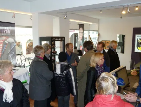 Besucherinnen und Besucher im Verkaufsraum vor einer Wand mit Sportbrillen.