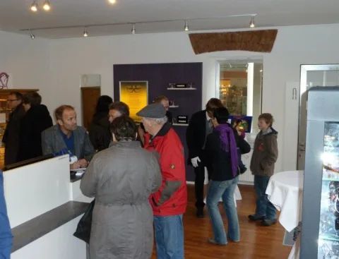 Gäste am Beratungstresen, dahinter die violette Wand mit beleuchteten Fassungsbrettern.