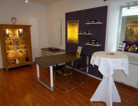 Beratungsplatz mit langem Tisch, Vitrinenschrank und einem Stehtisch mit weißer Husse.