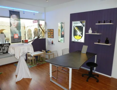 Der Werkstatt- und Anpassbereich mit Arbeitstisch vor violetter Wand.