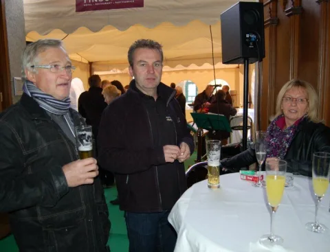 Drei Gäste mit Bier und Sekt an einem Stehtisch im Festzelt.