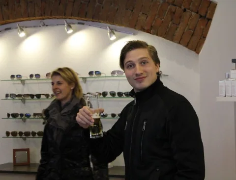 Zwei Gäste stoßen vor einer Wand mit Sonnenbrillen mit Sekt an.