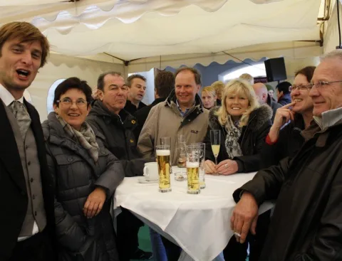 Eine Runde Gäste an einem Stehtisch mit Bier und Sekt.