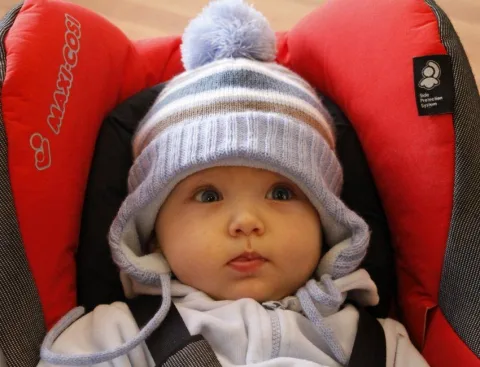 Ein Baby mit Streifenmütze im roten Autositz.