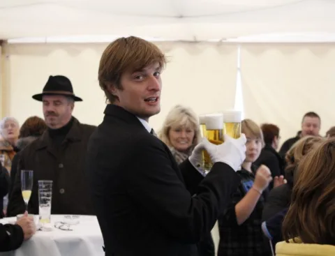 Ein Mitarbeiter trägt ein Tablett mit Biergläsern durch das volle Festzelt.