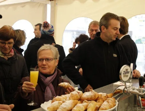 Am Buffet: eine Besucherin mit Orangensaft vor einer Platte mit Gebäck, daneben die Schankanlage.