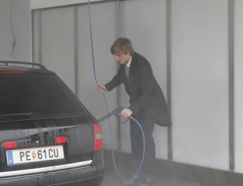 Ein Mitarbeiter im Anzug reinigt ein Auto mit dem Hochdruckreiniger.