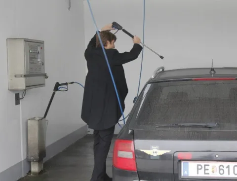 Ein Mitarbeiter im Anzug wäscht ein Auto in der Waschbox.