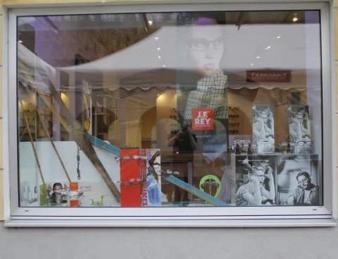 Das Schaufenster mit Werbeplakaten, darin spiegelt sich das Festzelt.