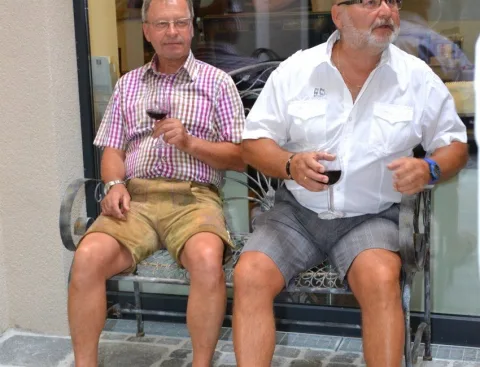 Zwei Gäste mit Gläsern auf einer Bank vor dem Haus