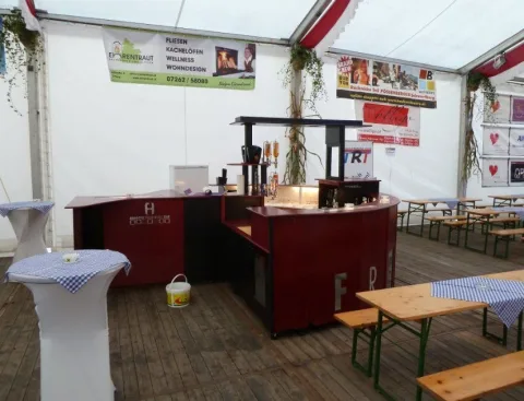 Die fertig aufgebaute Bar im Festzelt mit Stehtisch und Bierbänken davor, vor Beginn der Veranstaltung