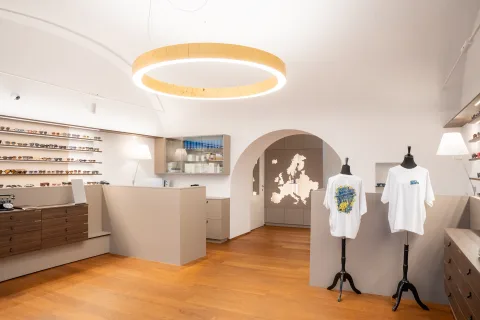 Verkaufsraum mit Lichtring an der Decke, der Europakarte im Rundbogen und zwei T-Shirts auf Ständern