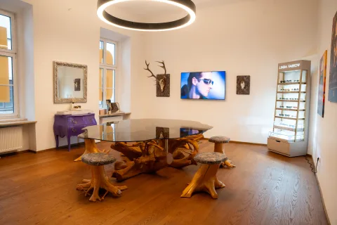 Wartebereich mit Tisch und Hockern aus Wurzelholz, einem Spiegel im Goldrahmen, einem Geweih und einem Bildschirm an der Wand