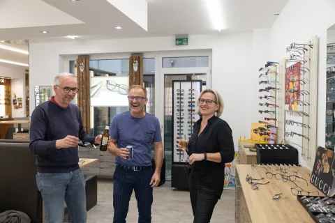 Beratungstische mit Bildschirmen vor einer langen Polsterbank, dahinter Brillenregale und der Eingang