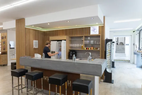 Die Theke aus Sichtbeton mit vier Barhockern, dahinter eine beleuchtete Vitrine und eine Kaffeemaschine
