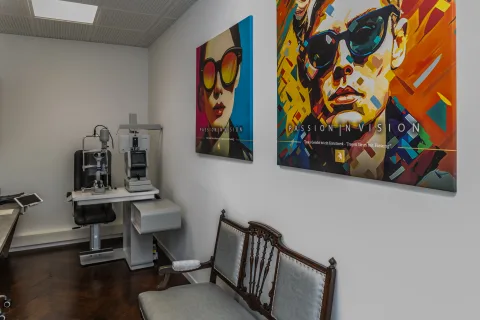 Untersuchungsraum mit Spaltlampe vor zwei großformatigen Pop-Art-Bildern, davor ein alter Holzstuhl