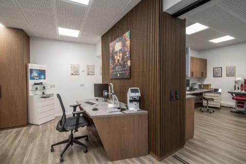Der Low-Vision-Arbeitsplatz: Schreibtisch mit Bildschirm und Vergrößerungsgerät vor einer Holzlamellenwand, dahinter der Untersuchungsbereich