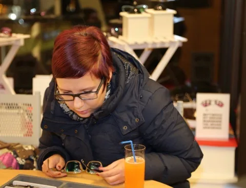 Eine Frau mit Brille sitzt mit einem Glas Orangensaft an einem Tisch