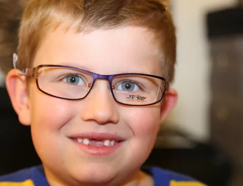 Ein kleiner Junge mit Brille und blauem Hemd lächelt in die Kamera