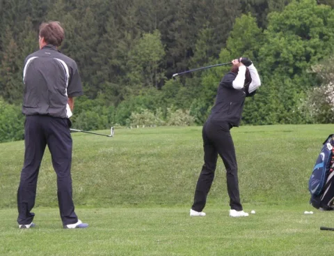 Zwei Spieler beim Abschlag vor dem Waldrand