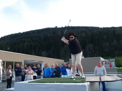 Ein Spieler beim Abschlag vor bewaldeten Hügeln