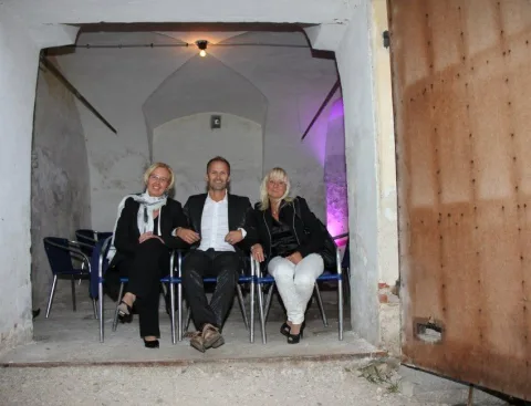 Drei Gäste an einem Tisch unter einem Gewölbebogen