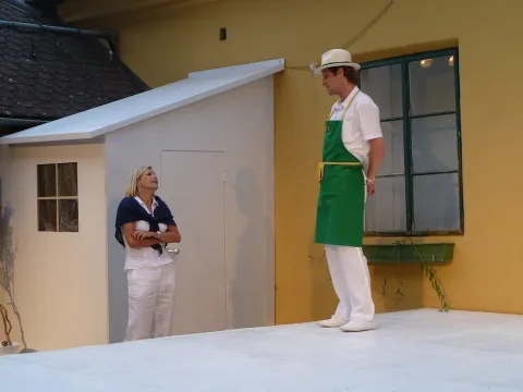 Ein Darsteller mit grüner Schürze auf einer Treppe, dahinter die Kulisse