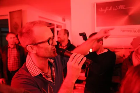 Ein Gast im rot beleuchteten Verkaufsraum zeigt lachend zur Seite.