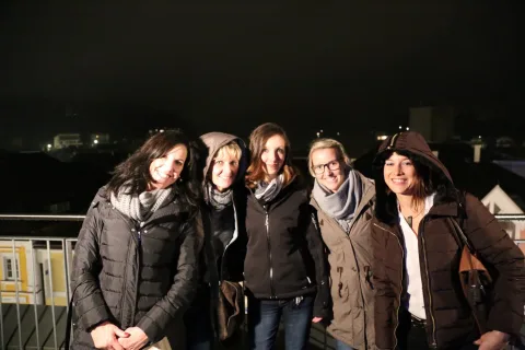 Fünf Frauen stehen abends nebeneinander auf der Terrasse über dem Ortszentrum.