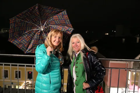 Zwei Frauen unter einem Regenschirm auf der Terrasse bei Nacht.