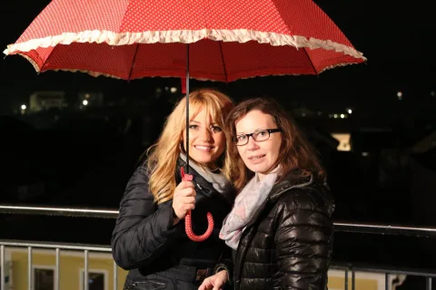 Zwei Frauen unter einem roten Regenschirm auf der Terrasse.