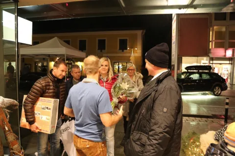 Gäste mit Geschenkkorb und Blumen vor dem beleuchteten Eingang.