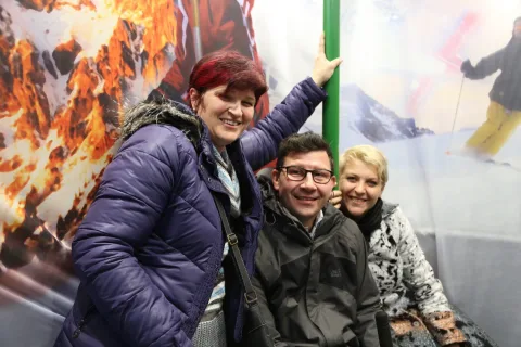 Drei Gäste posieren im Sessellift vor der Bergkulisse.
