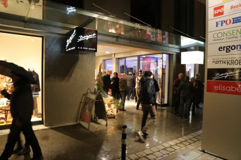 Die Einkaufsstraße bei Nacht mit beleuchteten Auslagen und Passanten.