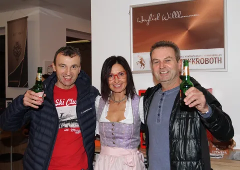 Drei Gäste mit Bierflaschen vor dem Willkommensplakat.