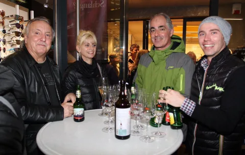 Vier Gäste an einem Stehtisch mit Wein und Gläsern.