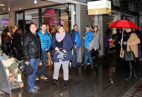 Passanten warten bei Regen vor dem Geschäft, eine mit rotem Schirm.