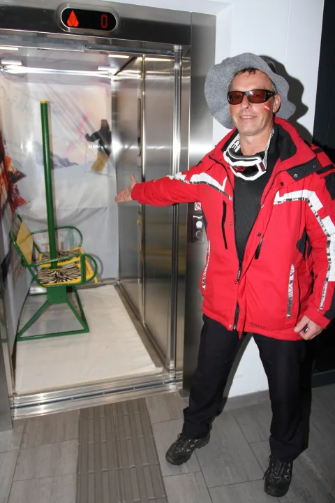 Ein Gast in roter Skijacke präsentiert den Sessellift im Aufzug.
