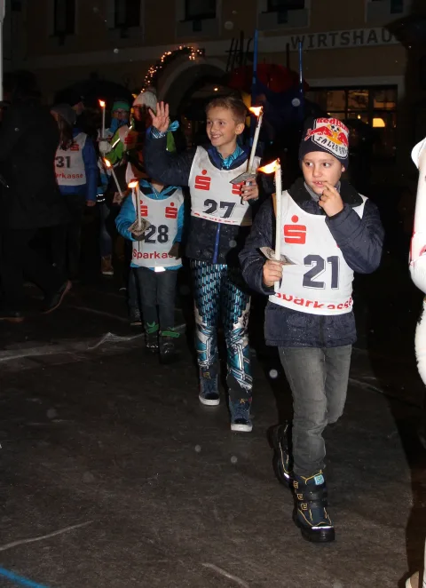 Kinder mit Startnummern tragen Fackeln durch die Straße.