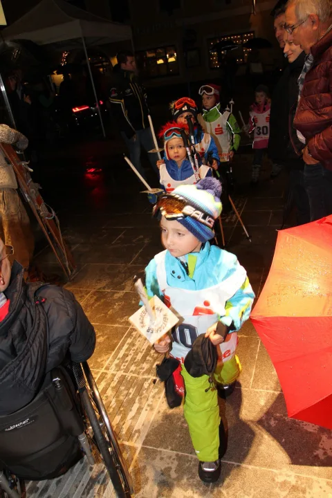 Kinder in Skibekleidung ziehen mit Fackeln durch die Straße.