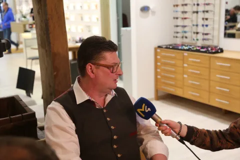 Ein Mann in Trachtenweste wird von einem Kamerateam interviewt, ein Mikrofon ist auf ihn gerichtet