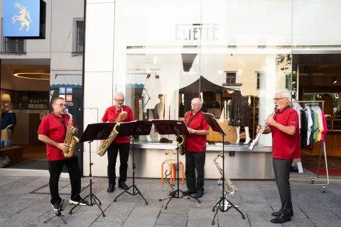 Vier Musiker in roten Hemden spielen mit Saxofon und Klarinette vor dem Geschäft