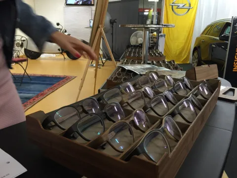 Eine Hand greift nach einer Brille aus einem Holztablett voller Modelle
