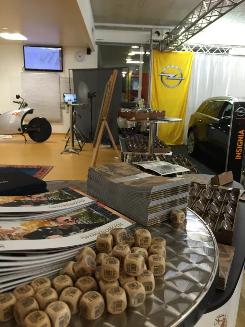 Prospektstapel auf einem Tisch, dahinter ein Fahrzeug im Autohaus