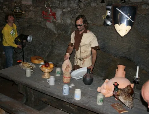 Ein Darsteller in mittelalterlichem Gewand an einer gedeckten Tafel mit Krügen und Schüsseln